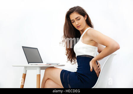 Kaukasische Mädchen mit chronischen Rückenschmerzen / Rückenschmerzen / Büro-Syndrom während der Arbeit mit Laptop auf weißen Schreibtisch über weißen Hintergrund isoliert Stockfoto