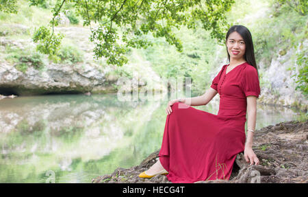 Modebewusste Frau sitzt neben einem Fluss allein Stockfoto