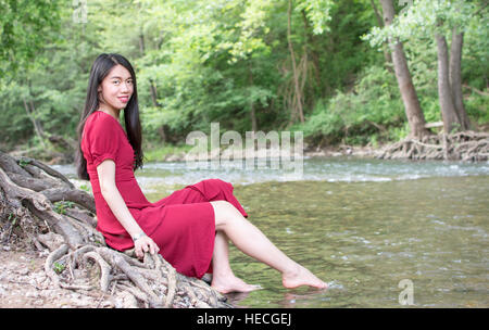 Modebewusste Frau sitzt neben einem Fluss allein Stockfoto