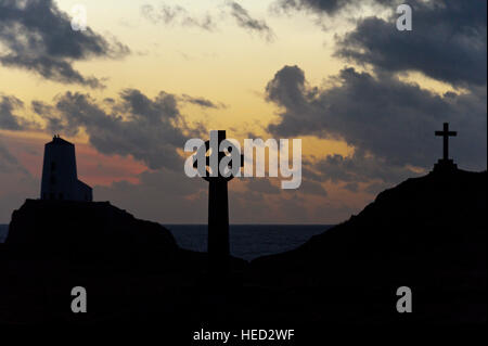 Newborough, Isle of Anglesey, Wales, UK. 21. Dezember 2016. Das Wetter.  Der alte Leuchtturm, einem keltischen Kreuz und St Dwynwens Cross sind Silhouette gegen die untergehende Sonne auf Llanddwyn Island, aka Ynys Llanddwyn am Abend der Wintersonnenwende der kürzeste Tag des Jahres 2016. Das Wetter.  (Tageslicht) Daylength heute in London, UK werden 7 Stunden 49 Minuten 40 Sekunden. © Graham M. Lawrence/Alamy-Live-Nachrichten. Stockfoto