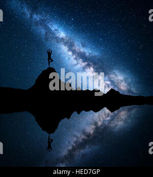 Milky Way. Silhouette einer stehenden Frau praktizieren Yoga auf den Berggipfel in der Nähe der See mit Himmel Spiegelung im Wasser Stockfoto