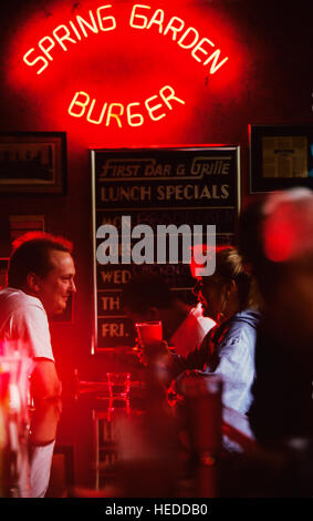 Ein Mann und eine Frau in einer Bar sprechen unter dem roten Neon-Licht eines Zeichens in einem Restaurant. Stockfoto