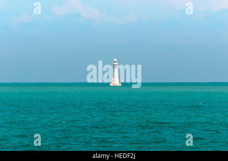 Weißer Leuchtturm mitten im Meer. Leuchtturm, umgeben von blauen Meerwasser und ein blauer Himmelshintergrund. Stockfoto