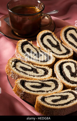 Einige Stücke der traditionellen ungarischen folk Kuchen Xmas Mohn Rollen - Bejgli auf einer Glasplatte und einer Tasse Tee Stockfoto