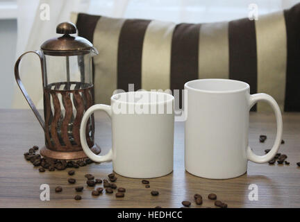 Zwei weiße Tassen, 11 und 15 oz, Mock-up. Gemütliche Atmosphäre, französische Presse, hölzernen Hintergrund, Kaffeebohnen für Dekorationen. Stockfoto