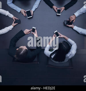 Geschäftsleute mit Smartphones sitzen um den Tisch, Ansicht von oben Stockfoto