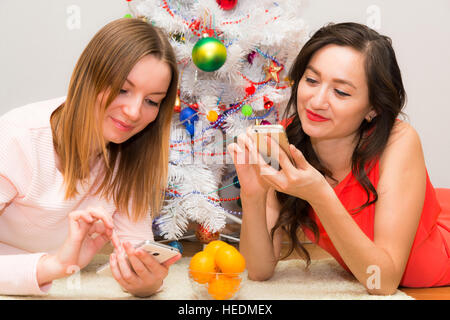 Weihnachtszeit, zwei lächelnde junge Mädchen lag auf dem Teppich im Hintergrund einen Weihnachtsbaum beleuchtet Stockfoto