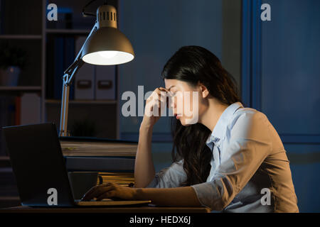 Asien-Geschäftsfrau sitzen am Schreibtisch Kopfschmerzen Überstunden arbeiten spät in die Nacht. im Innenbereich Office-Hintergrund Stockfoto