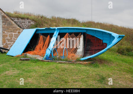 Kleine offene Fischerboot mit Netzen und Lobster Pot erhalten für die Nachwelt vor einem kleinen Fischer Geschäft in Kinloss, Schottland Stockfoto