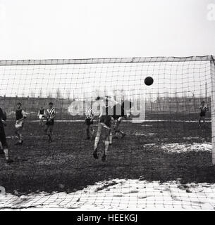 1965, historische, Winter und einem Amateur Football Spiel auf verschneiten Pitch, ein Verteidiger auf der Linie springt, um zu versuchen, den Ball ins Netz für ein Ziel zu gehen und zu vermeiden. Stockfoto