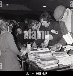 1965, historisch, Menschen suchen oder stöbern Sie durch die verschiedenen Bücher und Plunders auf einem Flohmarkt-Stand zur Verfügung. Stockfoto