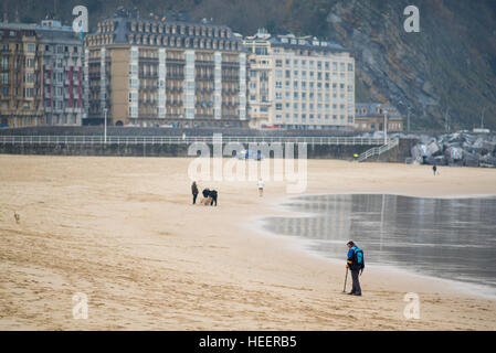 Ein Mann verwendet einen Metalldetektor auf Zurriola Strand, San Sebastian, im winter Stockfoto