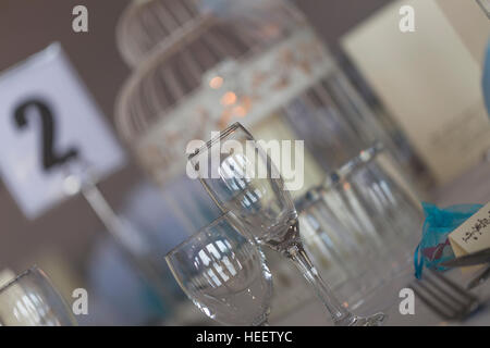 Esstisch set für Hochzeitsfeier mit Champagner und Wein Gläser, Besteck, Tischnummer und Kerze im Vogelkäfig Stockfoto