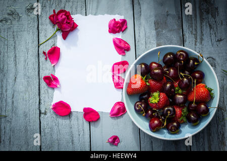 Eine Schale mit Kirschen und rote Rosen auf hölzernen Hintergrund Stockfoto