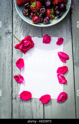 Eine Schale mit Kirschen und rote Rosen auf hölzernen Hintergrund Stockfoto