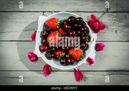 Eine Schale mit Kirschen rote Rosen auf hölzernen Hintergrund Stockfoto
