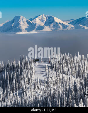 Schneebedeckte Berggipfel mit Skilift an der Spitze eines anderen. Frische Schneedecke auf Bäume und Nebel oder Wolke Schicht zwischen. Stockfoto