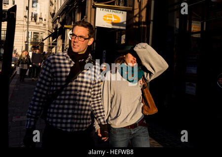 Ein junges Paar, ein Spaziergang entlang einer Londoner Straße in der Abenddämmerung. Die Frau ist die Augen von die tiefstehende Sonne Abschirmung. Stockfoto