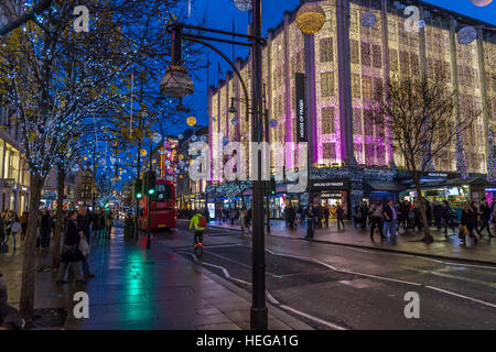 Weihnachtseinkäufer, die zur Weihnachtszeit am House of Fraser auf der Londoner Oxford Street vorbeilaufen und von Weihnachtslichtern überzogen sind, Oxford Street, London, Großbritannien Stockfoto