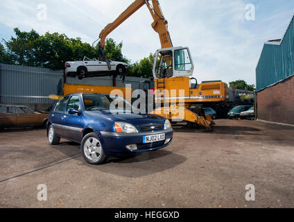 2002 Ford Fiesta bei einem Breakers Yard, ist eine Schrott Umgang mit Greifer Greifer ein mk3 Vauxhall Cavalier in den Brecher dahinter zu heben Stockfoto