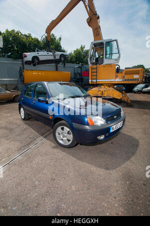 2002 Ford Fiesta bei einem Breakers Yard, ist eine Schrott Umgang mit Greifer Greifer ein mk3 Vauxhall Cavalier in den Brecher dahinter zu heben Stockfoto