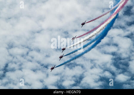 Rote Pfeile mit rot, weiß und blauer Rauch an einem bewölkten, blauen Himmel. Stockfoto