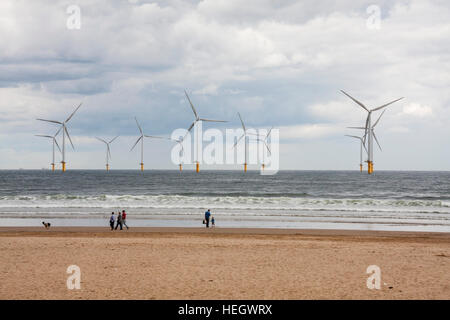 Redcar Strand an der Küste von Nordostengland mit offshore Windenergieanlagen und Menschen zu Fuß am Strand entlang Stockfoto