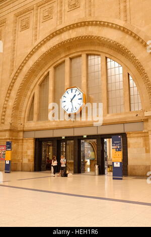 Der Eingang und Foyer in Leipzig, Deutschland-Bahnhof.  Ein paar unterhält sich unten eine riesige Uhr, die über ihnen hängen. Stockfoto