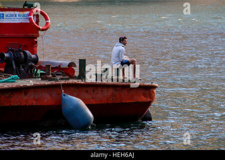 Ein Mann in Shorts und Flip-Flops ist vom Deck eines roten Workboat in einem norwegischen Fjord Angeln. Stockfoto