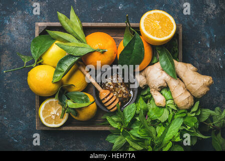 Zutaten für die Herstellung von Immunität, die Steigerung der natürlichen Getränk. Zitronen, Orangen, Minze, Ingwer, Honig in Holzkiste über Sperrholz Hintergrund, Ansicht von oben. Sauber ea Stockfoto