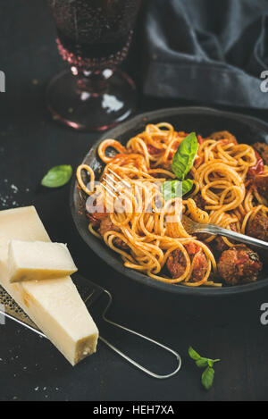 Italienische Pasta-Essen. Spaghetti mit Meatballas, Basilikum und Parmesan Käse in dunkle Platte und Rotwein im Glas auf schwarzem Hintergrund, selektiven Fokus. Stockfoto