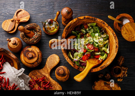 Salat aus frischem Gemüse in Olivenöl Holz Schüssel und hölzernen Geschirr auf schwarz verbrannten Holz Hintergrund