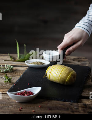 Hasselback Kartoffeln: zarte Frauenhand schneiden eine Kartoffel auf Holztisch Stockfoto