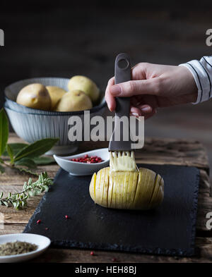 Hasselback Kartoffeln: zarte Frauenhand Bürsten eine Kartoffel mit Butter Stockfoto