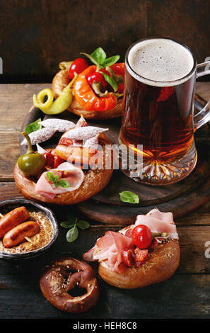 Vielzahl von Fleischsnacks gebratene Würstchen, kuckt, Schinken, eingelegte Chilischoten in gesalzenen Brezeln serviert mit frischem Basilikum und Glas Lagerbier ov Stockfoto