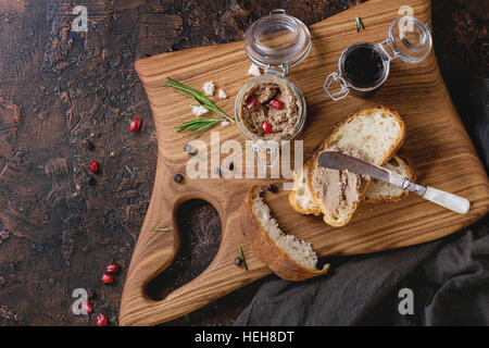 Gläsern Huhn Leber Pastete mit schwarzer Johannisbeere Marmelade, Granatapfel Korn und Schnittbrot, serviert mit Vintage Messer auf Schneidbrett aus Holz über da Stockfoto