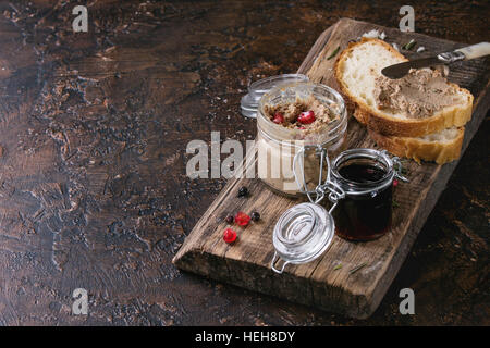 Gläsern Huhn Leber Pastete mit schwarzer Johannisbeere Marmelade, Granatapfel Korn und Schnittbrot, serviert mit Vintage Messer auf Schneidbrett aus Holz über da Stockfoto