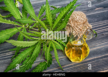 Cannabis-Blätter und Öl in Glasflasche auf hölzernen Hintergrund Stockfoto