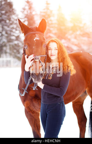 Junge Teenager-Mädchen stehend mit Bucht Pferd in Winter Park bei Sonnenuntergang Stockfoto