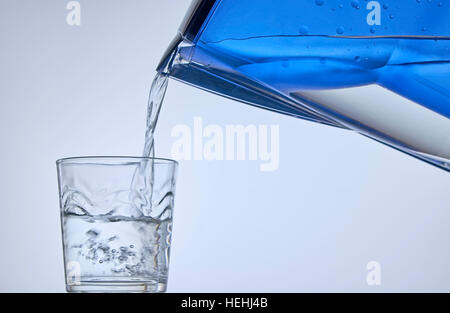 Nahaufnahme des strömenden Wassers in Glas auf der linken Seite aus blauem Wasser Filter Krug auf der rechten Seite. Stockfoto