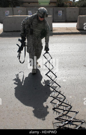 090213-N-0917W-067 US Armee Pfc. Walters von der 2. Brigade, 1st Infantry Division richtet ein Spike Streifen an einem Fahrzeug Kontrollpunkt in Ameriyah, Irak, am 13. Februar 2009.  DoD-Foto von Petty Officer 2. Klasse Robert J. Whelan, US Navy.  (Freigegeben) US Armee-Spike-Streifen Stockfoto