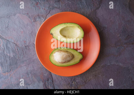 Avocado-Hälften liegen auf einer orange Platte auf eine horizontale Schiefer Stockfoto