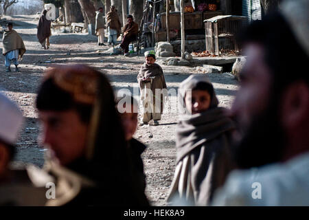 Eine Linie erstreckt sich auf die Straße, als ein afghanischer Junge neugierig während eine kostenlose Klinik außerhalb der Mannakhil umfassenden Health Care Center im Sherzad Bezirk im Osten Afghanistans Nangarhar Provinz 26. Dezember Uhren. Soldaten, die 1. Staffel, 61. Kavallerie-Regiment, Task Force Panther zugewiesen arbeitete eng mit Pendants Afghan National Army, Hilfe für die Bewohner in der Umgebung zu leisten. Patienten Line-up für Pflege in Sherzad 354187 Stockfoto