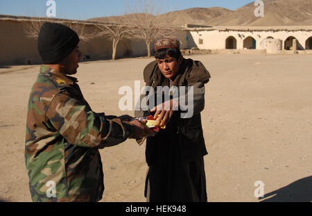 Eine afghanische Commando von 2. Kompanie, 3. Commando Kandak Hände Süßigkeiten kaufte er von einem lokalen Shop für ein Kind während einer Operation 8. Februar 2011, in Shah Wali Kot District, Provinz Kandahar, Afghanistan. Die Kommandos wurden von Dorfbewohner während des Betriebes begrüßt, da sie Nahrung und Schutz während ihrer Mission ganztägigen angeboten wurden. Sie, inhaftiert, zusammen mit District Chief der Polizei Bacha Khan, 20 mutmaßliche Aufständische in dem Bemühen, die Aufständischen Einschüchterung in der Gegend nicht mehr in Frage zu stellen. Die Kommandos sind eine Partnerschaft mit US-Militärangehörige von Special Operations Task Force - South. Afghanische C Stockfoto