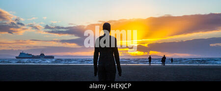 Crosby, Merseyside, England.  Großbritannien Wetter. Kalten & Blustery als festliche Antony Gormley Iron Man Statue blickt auf das Meer und den Sonnenuntergang über der walisischen Küste.  Diese barnacled lebensgroße Kunstschaffens ist einer der 100 Replikate des Künstlers platziert entlang der Länge des Crosby Strand mit Blick auf die Mündung des Flusses Mersey und der wichtigsten Schifffahrtswege, und aus dem Hafen von Liverpool. Bildnachweis: MediaWorldImages/Alamy Live-Nachrichten Stockfoto