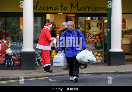 Brighton UK 23. Dezember 2016 - beladen mit Taschen Shopper pass von einem Big Issue Verkäufer als Weihnachtsmann verkleidet, beim Verlassen eines Safeway-Supermarkts in Brighton mit heute voraussichtlich die verkehrsreichsten Weihnachts-Essen shopping-Tag der festlichen Zeit in Großbritannien Credit: Simon Dack/Alamy Live News Stockfoto