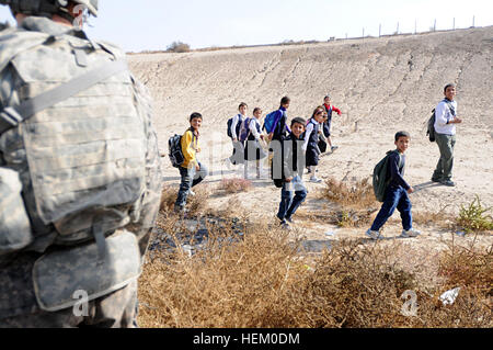 Irakische Kinder zu Fuß zur Schule Lächeln wie sie eng von Fallschirmjägern Pass, die 2. Brigade zugewiesen, ziehen 82nd Airborne Division A Truppe, 1. Staffel, 73. Kavallerie-Regiment, Sicherheit auf einer großen Konvoi-Route in Bagdad. Die Fallschirmjäger zog Sicherheit für andere Einheiten der Brigade von Camp Ramadi zu Kuwait reisen. Die Truppe hat mehrere Haltestellen entlang der Strecke, überprüfen den Bereich zu Fuß für improvisierte Sprengsätze und Treffen mit irakischen Armeesoldaten an IA Checkpoints. Die 2. Brigade ist die letzte Brigade in Bagdad und fördert den Rückzug der US-Streitkräfte aus Stockfoto