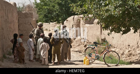 Ein Soldat des 1. Platoon, Bravo Kompanie, 1. Bataillon, 23. Infanterieregiment, hält am 23. Juni 2012 eine Patrouille in Naib Kalay, Afghanistan, an, als sich die Kinder der Gegend versammeln. Soldaten tragen oft kleine Leckerbissen bei sich, was die Beziehungen zwischen den Gemeinden stärkt und ein positives Engagement mit der lokalen Bevölkerung während der Patrouillen fördert. Stockfoto