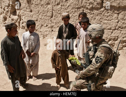 Ein Soldat des 1. Platoon, Bravo Kompanie, 1. Bataillon, 23. Infanterieregiment, verteilt Trauben an einheimische Kinder während einer Patrouille in der Region Naib Kalay in Afghanistan und trägt kleine Leckereien im Rahmen der Routineeinsätze mit Gemeinden. Stockfoto