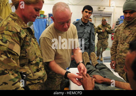 Marine Kapitän Stephen Dirusso, nach vorn Operationsteam zuständigen Offizier, untersucht Mohammed Qasim, ein afghanischer uniformierten Polizisten mit der 4. Firma Reserve Kandak vor seiner Operation auf Forward Operating Base Lagman, Afghanistan, am 13. Dezember 2012.  Qasim wurde zwei Monate zuvor durch einen improvisierten Sprengsatz verletzt und wurde von den Hawaii National Guard Sicherheit Kräfte Advisory Team 21, die Partner mit Qasim Einheit Lagman FST gebracht.  (US Armee-Foto von Sgt. Lori Bilyou) Afghanischer Polizist geholfen durch SFAT, FST 121213-A-BF245-305 Stockfoto